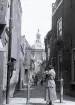 Foto av en gränd med en kvinna längst fram i bild och där man i bakgrunden kan se kyrkan Marekerk i Leiden , Nederländerna, 1924-25.