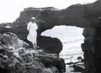 Foto av en kvinna som står vid en klippformation vid vattnet, troligen någonstans på franska atlantkusten, 1924-25.