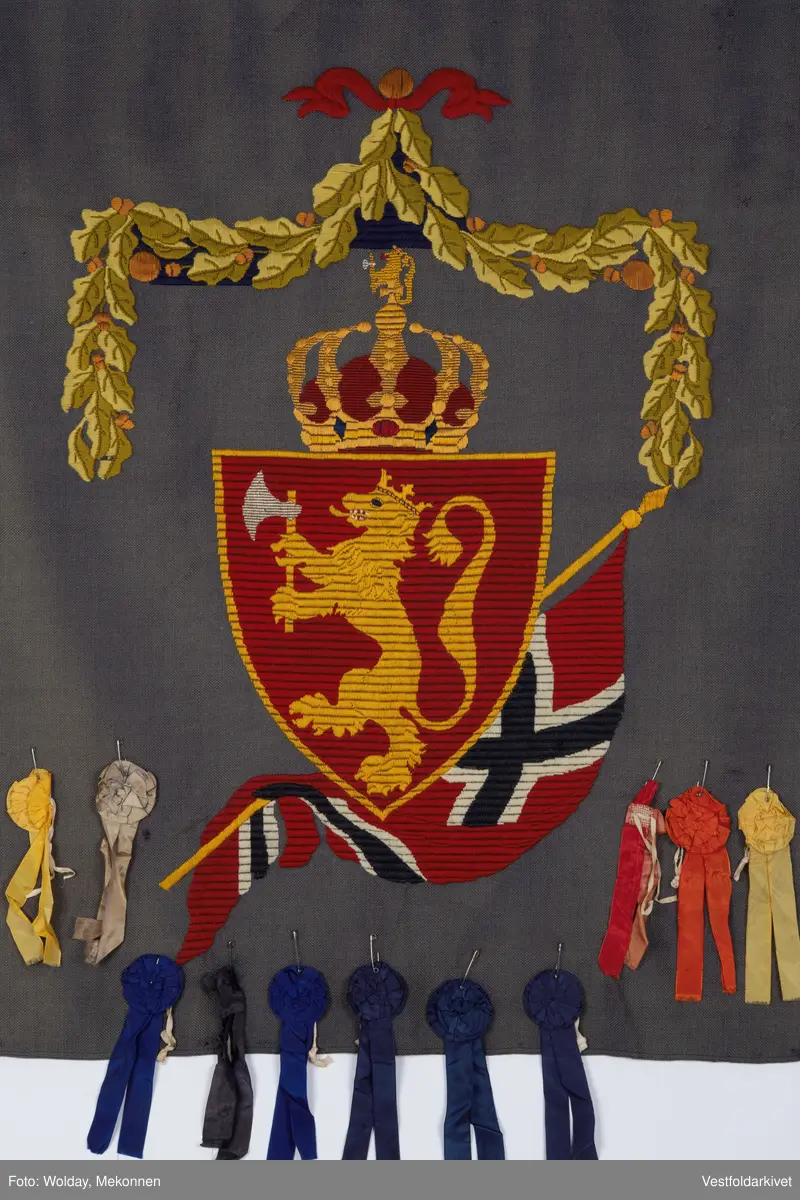 Blått veggteppe med riksvåpenet, påfestet rosetter 