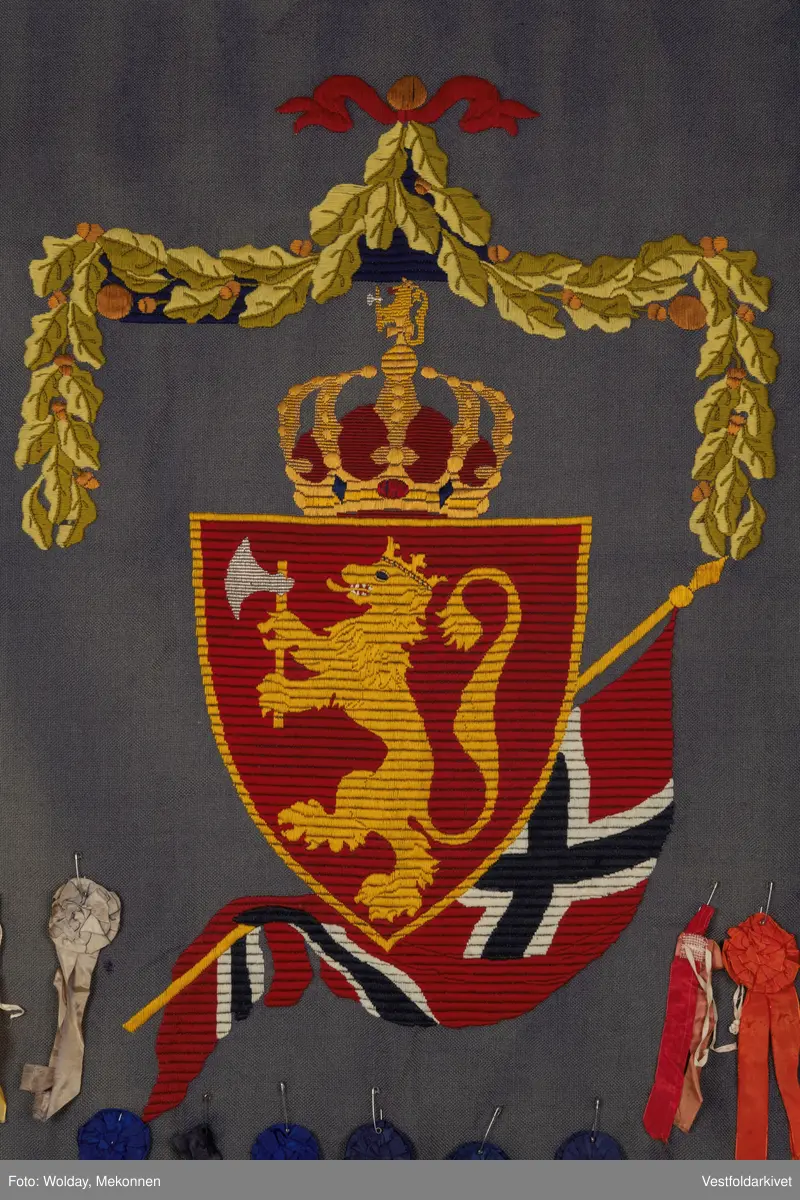 Blått veggteppe med riksvåpenet, påfestet rosetter 