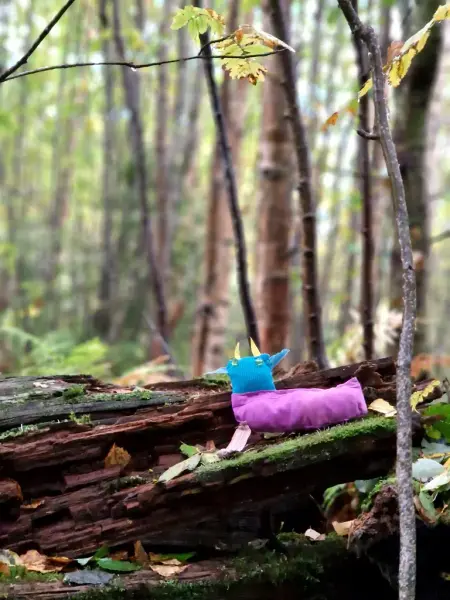 En tygfigur står på en murken stock ute i skogen.