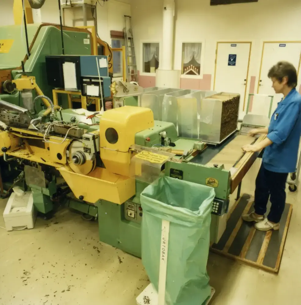 Kvinna i blått som står vid maskin i en fabrik.