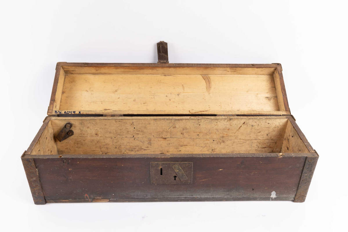 Verktøykasse i tre med hengslet lokk. To stk. håndtak i metall på kortsidene, samt metallbeslag montert på hjørner. I front er det monter hengsel til lås.