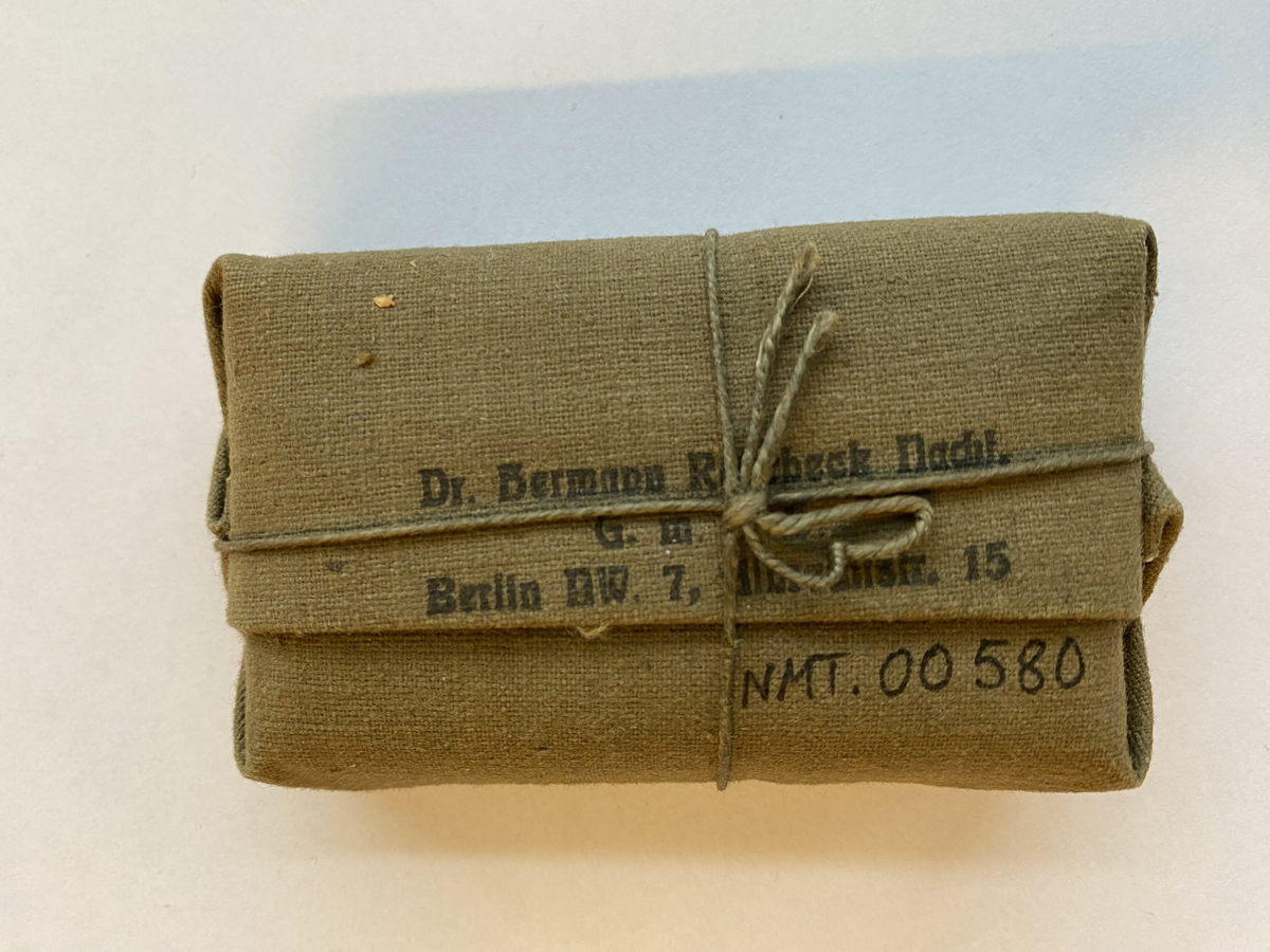 Ein bandasjeforpakning med informasjon trykt på tekstilen. Innpakka i stoff med band rundt.