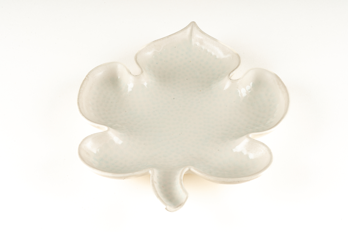 Saladjär av flintgods, modell -EB eller -YT, formgiven av Arthur Percy för Gefle Porslinsfabrik. Skålat, stiliserat lönnlöv med svängd stjälk, femflikigt. Femflikig fotring. Dekor, ljusgrön ton på ovansidan mot vit glasyrfond. Brun skorstensstämpel under med text "Gefle Sweden Percy".