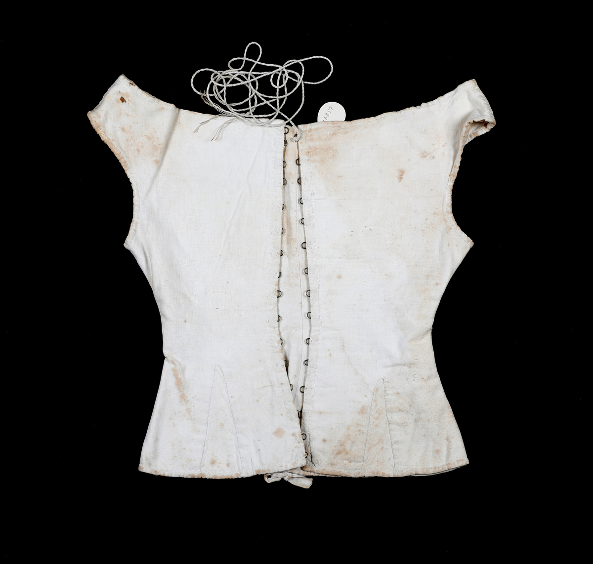 Liv eller korsett av lin med metallhekter og tvunnet tråd til snøring. Det har søm midt bak med hempe oppe og nede. Sidesømmen er litt tilbaketrukket, og det er felt inn stoff neders i sida for utsving fra livet. Halsåpningen er båtformet.