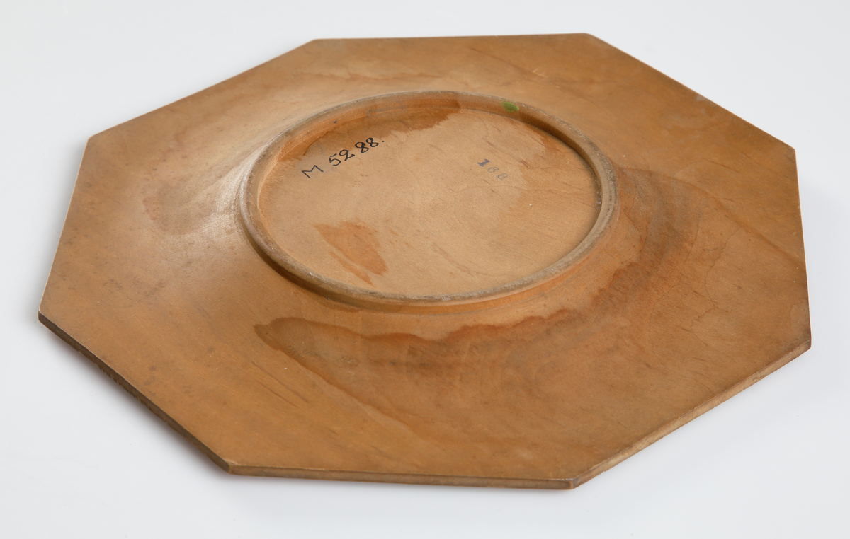 Trätallrik, åttkantig med glödritad och målad dekor i form av linnéor.

Inskrivet i huvudkatalog 1932.