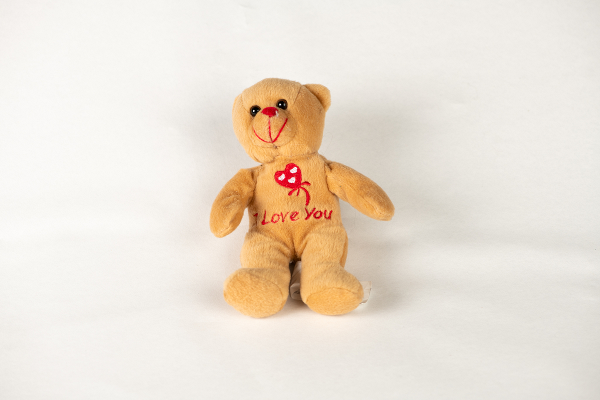 Liten, brun bamse, med teksten "I Love you" og hjerteform sydd på magen.