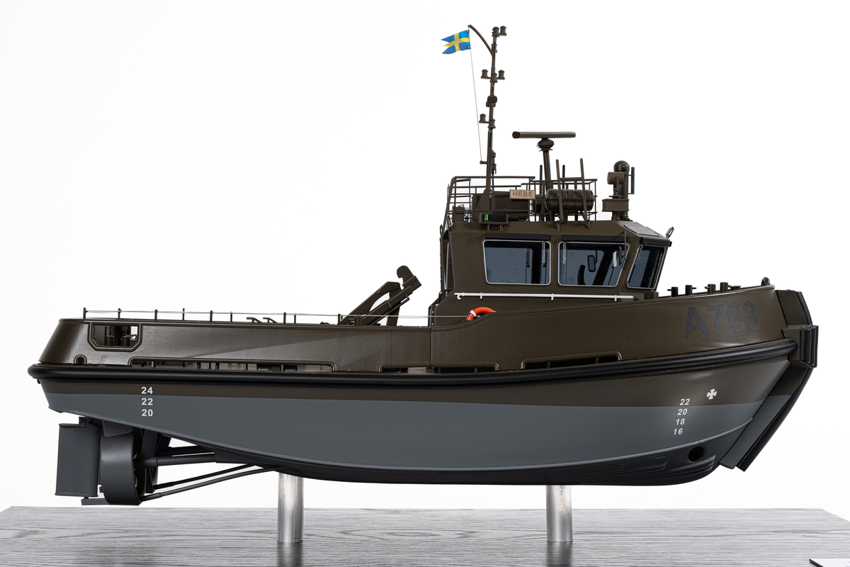 Fartygsmodell föreställande hamnbogseraren Hebe. Modell av metall och plast på två stöd. Monterbotten av mörkt trä samt plexiglashuv. Fartygsskrovet gråmålat under vattenlinjen samt militärgrönt upptill. Märkt i svart: "A763". Baktill en lyftkran. Namnbrädor som anger att det är Hebe.

En skylt som anger tillverkare: "Scale modells Weston ltd". En skylt som anger mått samt texten: "A763 STU 1706 ICE DAMEN 2024".