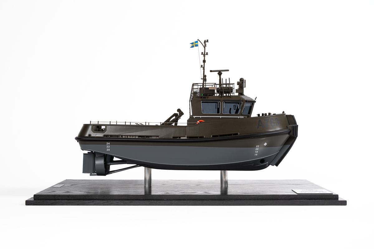 Fartygsmodell föreställande hamnbogseraren Hebe. Modell av metall och plast på två stöd. Monterbotten av mörkt trä samt plexiglashuv. Fartygsskrovet gråmålat under vattenlinjen samt militärgrönt upptill. Märkt i svart: "A763". Baktill en lyftkran. Namnbrädor som anger att det är Hebe.

En skylt som anger tillverkare: "Scale modells Weston ltd". En skylt som anger mått samt texten: "A763 STU 1706 ICE DAMEN 2024".