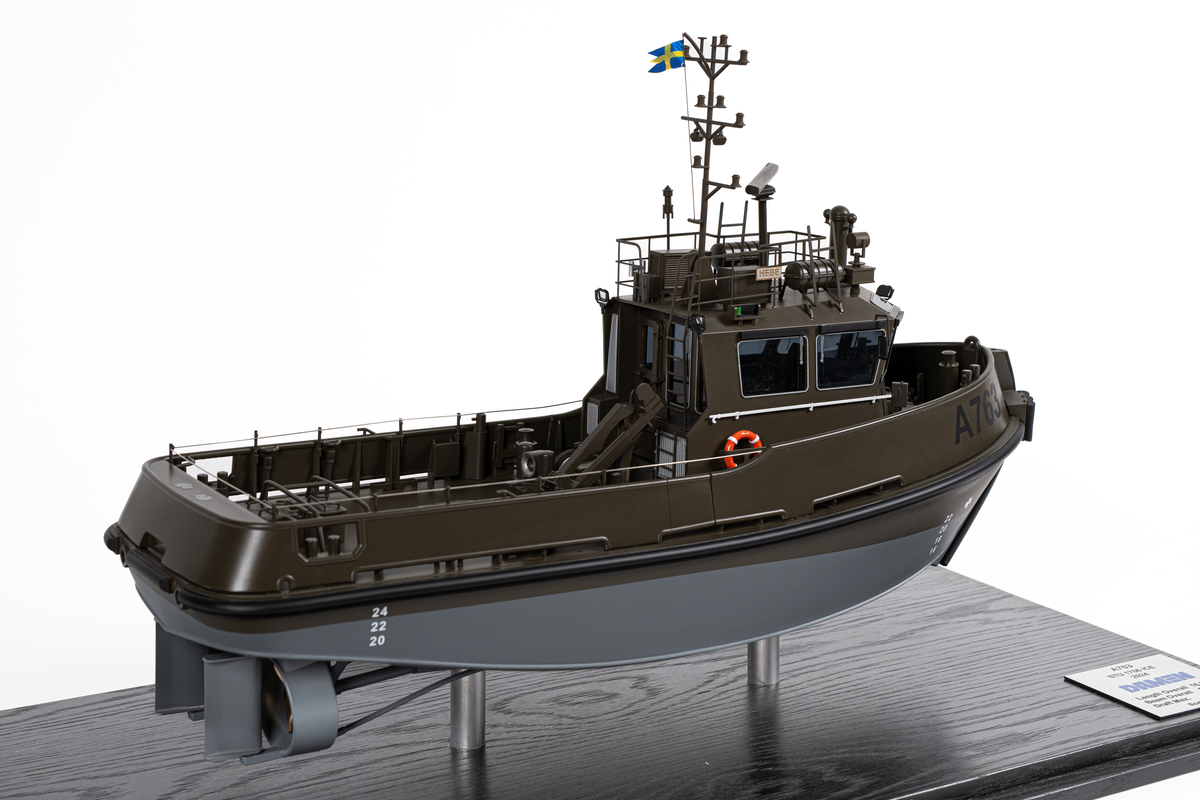 Fartygsmodell föreställande hamnbogseraren Hebe. Modell av metall och plast på två stöd. Monterbotten av mörkt trä samt plexiglashuv. Fartygsskrovet gråmålat under vattenlinjen samt militärgrönt upptill. Märkt i svart: "A763". Baktill en lyftkran. Namnbrädor som anger att det är Hebe.

En skylt som anger tillverkare: "Scale modells Weston ltd". En skylt som anger mått samt texten: "A763 STU 1706 ICE DAMEN 2024".