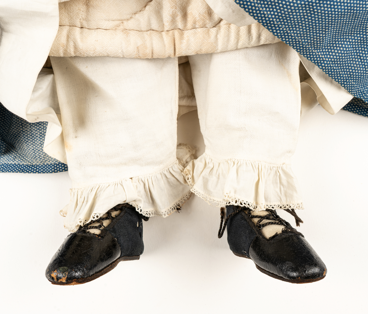 Docka, "Fedora", kroppen är svarvad av prosten Carl Steffenburg, Sundborn (född 1799), är iklädd linne, snörliv, byxor, stupp, tre underkjolar och blå klänning med vita prickar.
Kjolen har två volanger, skörtet på livstycket bildar en tredje volang.