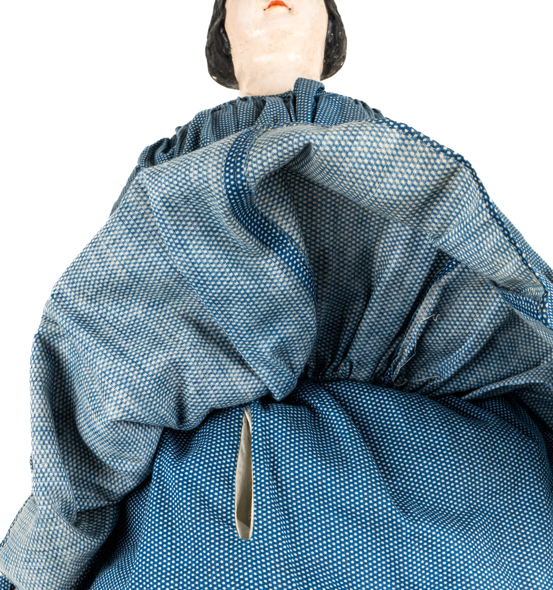Docka, "Fedora", kroppen är svarvad av prosten Carl Steffenburg, Sundborn (född 1799), är iklädd linne, snörliv, byxor, stupp, tre underkjolar och blå klänning med vita prickar.
Kjolen har två volanger, skörtet på livstycket bildar en tredje volang.