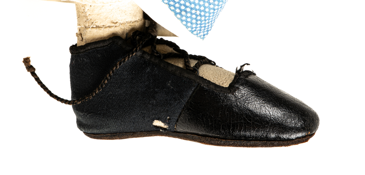 Docka, "Fedora", kroppen är svarvad av prosten Carl Steffenburg, Sundborn (född 1799), är iklädd linne, snörliv, byxor, stupp, tre underkjolar och blå klänning med vita prickar.
Kjolen har två volanger, skörtet på livstycket bildar en tredje volang.