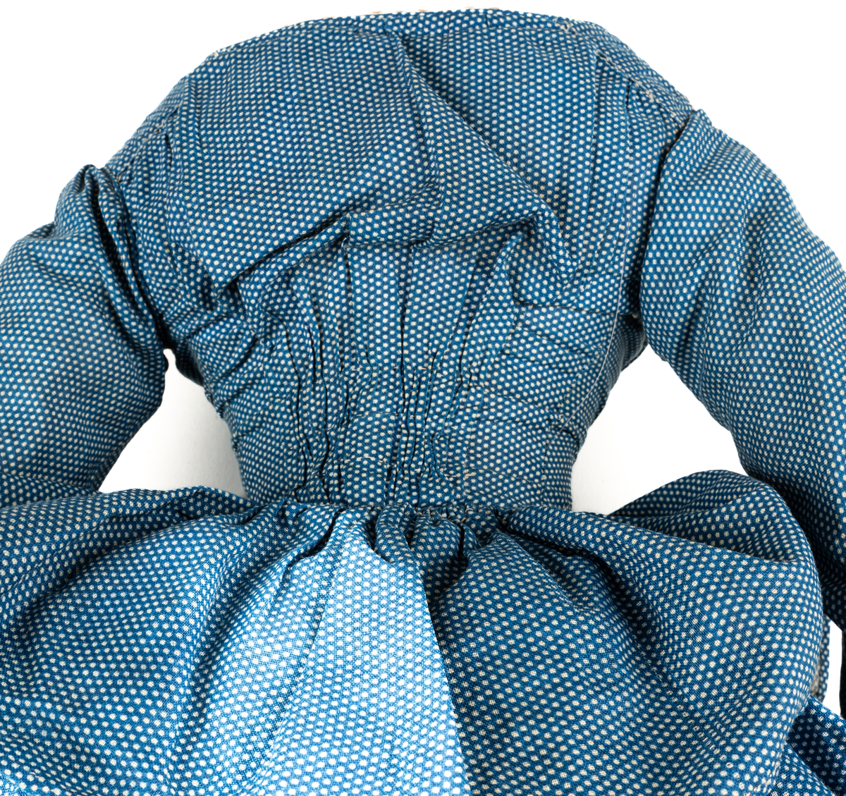 Docka, "Fedora", kroppen är svarvad av prosten Carl Steffenburg, Sundborn (född 1799), är iklädd linne, snörliv, byxor, stupp, tre underkjolar och blå klänning med vita prickar.
Kjolen har två volanger, skörtet på livstycket bildar en tredje volang.