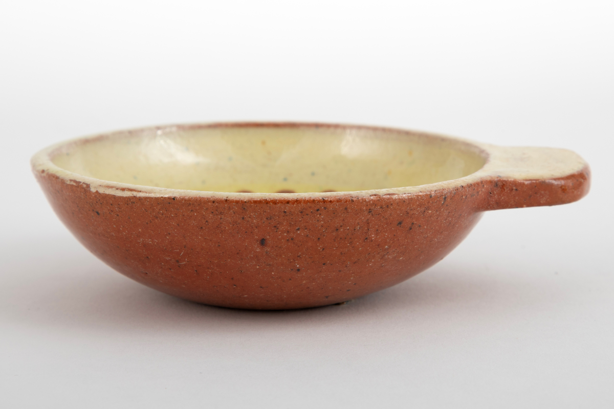 Kabaretskål av dreid leirgods. Skålene er runde med en enkel flat hank. På innsiden har skålen gulhvit glasur og er dekorert med en grønne gren.