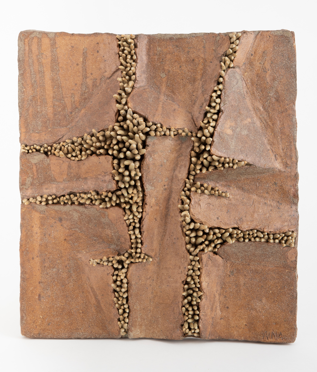 Kvadratisk plate i glasert steingods. På platen ser vi "tentakler" som bryter seg gjennom leira, hever den og danner sprekker i flaten. Utmeislet på undersiden med feste for oppheng.