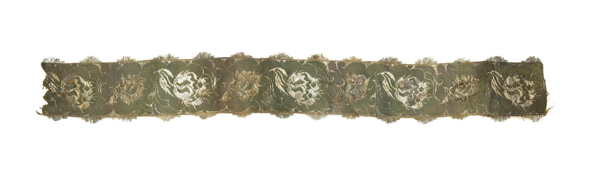 To deler bånd med tilhørende sløyfe. Vevd av silketråd, bomull(?), og metalltråder av antatt gull og sølv, med floralt mønster, typisk for rokokkoperioden. På den ene siden, antatt framsiden(?), er stoffet grønnfarget med florale motiver av metalltråd. På den andre siden, ses tydelige  fargede tråder av grønn, gul og rød silke/bomull.

Løkker av metalltråd, antatt sølv og/eller gull, langs begge langsidene av båndet. Gjennom hele båndet finner man rester av knappenåler av kobber som er korrodert. 

Sløyfen har tilnærmet lik mønstring og farger, og er antagelig formet av samme type bånd som hårbåndene.