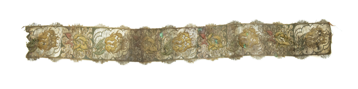 To deler bånd med tilhørende sløyfe. Vevd av silketråd, bomull(?), og metalltråder av antatt gull og sølv, med floralt mønster, typisk for rokokkoperioden. På den ene siden, antatt framsiden(?), er stoffet grønnfarget med florale motiver av metalltråd. På den andre siden, ses tydelige  fargede tråder av grønn, gul og rød silke/bomull.

Løkker av metalltråd, antatt sølv og/eller gull, langs begge langsidene av båndet. Gjennom hele båndet finner man rester av knappenåler av kobber som er korrodert. 

Sløyfen har tilnærmet lik mønstring og farger, og er antagelig formet av samme type bånd som hårbåndene.