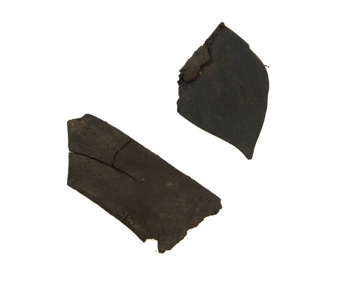 En sløyfe av brokade, antagelig av silkestoff og gull- og/eller tråd. Midten av sløyfen er presset og sydd sammen av tykk tråd (av bomull?). Den ene siden har grønt og rødaktig fargeskjær, de florale mønstrene er av metalltråd. Den andre siden har tydeligere fargesammensetninger i trådene - rød, gul og noe lilla. Løkker av metalltråd langs kantene. Taggete ender på sløyfa.

To lærfragmenter - den ene er avlang, og den andre tilspisset.