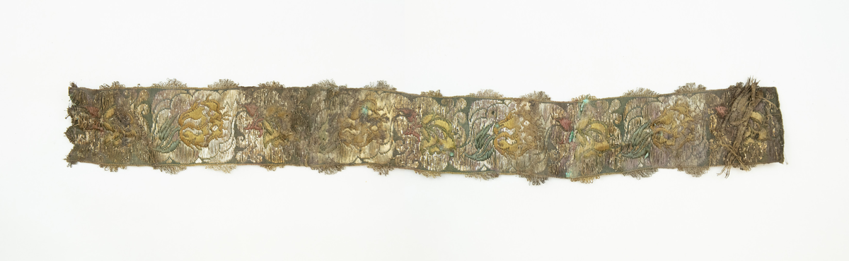 To deler bånd med tilhørende sløyfe. Vevd av silketråd, bomull(?), og metalltråder av antatt gull og sølv, med floralt mønster, typisk for rokokkoperioden. På den ene siden, antatt framsiden(?), er stoffet grønnfarget med florale motiver av metalltråd. På den andre siden, ses tydelige  fargede tråder av grønn, gul og rød silke/bomull.

Løkker av metalltråd, antatt sølv og/eller gull, langs begge langsidene av båndet. Gjennom hele båndet finner man rester av knappenåler av kobber som er korrodert. 

Sløyfen har tilnærmet lik mønstring og farger, og er antagelig formet av samme type bånd som hårbåndene.