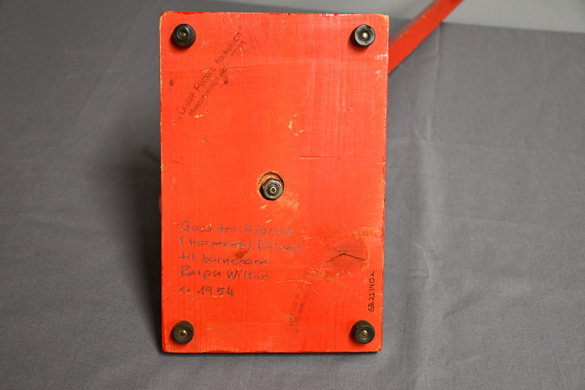 Rød og grønn høy kran i tre med bred base. Kan roteres 360 grader. Håndtakt i lær på bakparten, sveiv på toppen og hasp på høyre side.