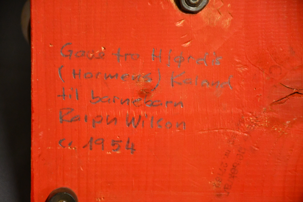 Rød og grønn høy kran i tre med bred base. Kan roteres 360 grader. Håndtakt i lær på bakparten, sveiv på toppen og hasp på høyre side.