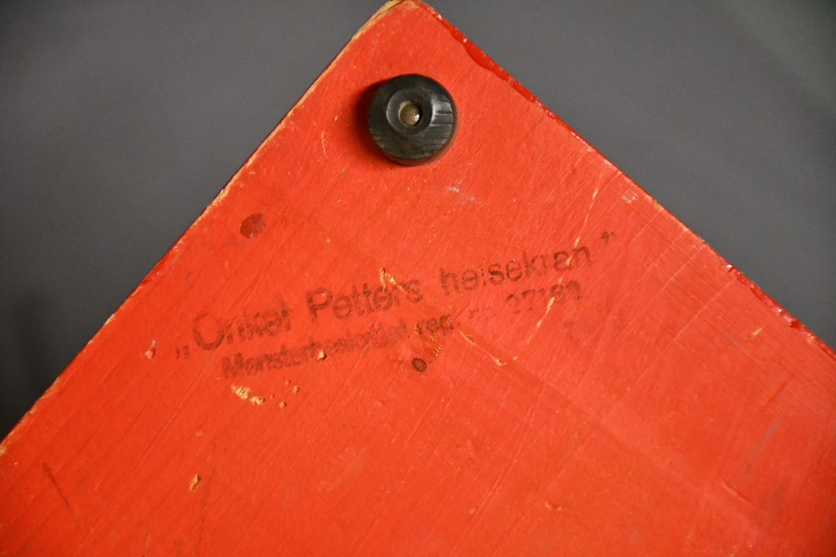 Rød og grønn høy kran i tre med bred base. Kan roteres 360 grader. Håndtakt i lær på bakparten, sveiv på toppen og hasp på høyre side.