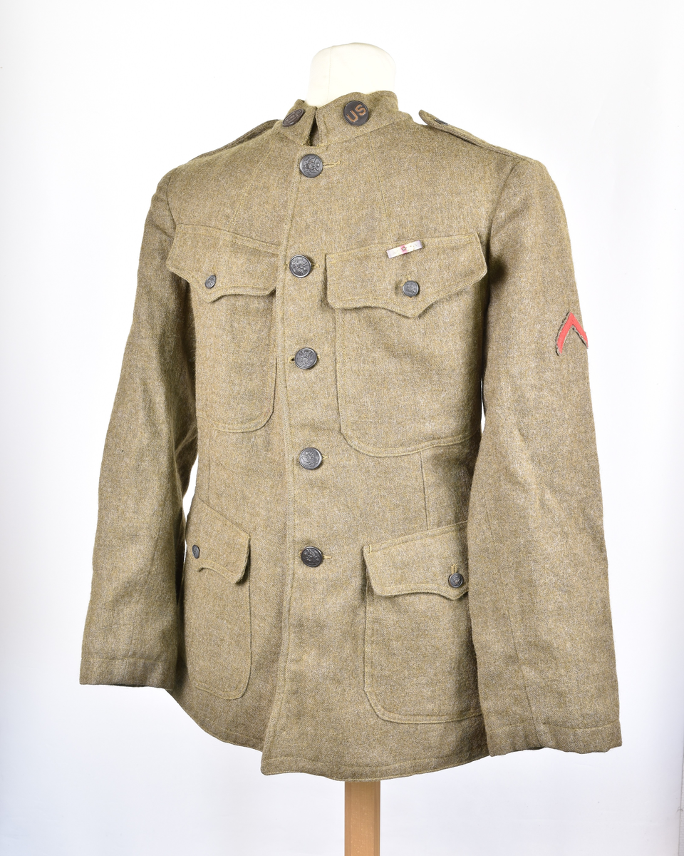 Grønn uniformsjakke i ull fra første verdenskrig. Fire knapper med ørnemotiv foran, samt to knapper på kragen.