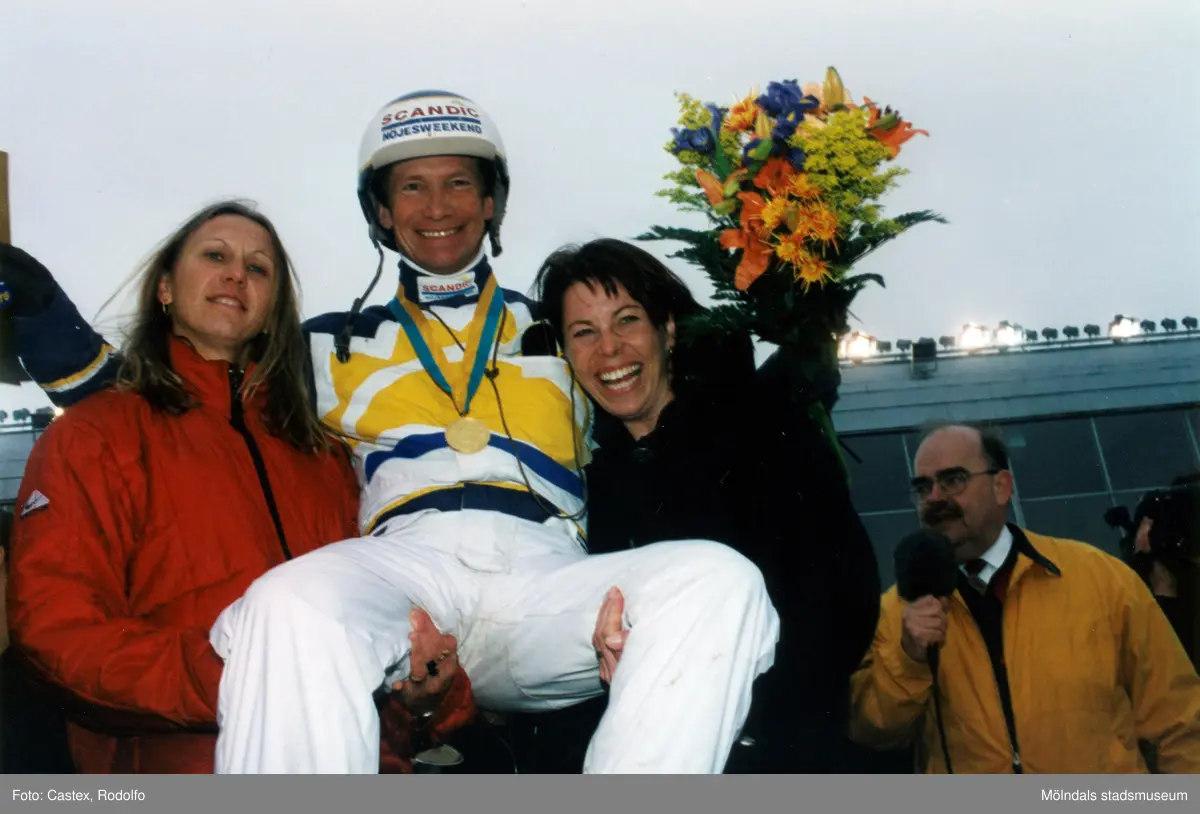 Skidskytten Magdalena Forsberg och friidrottaren Ludmila Engquist bär upp den segrande travkusken i samband med Olympiatravet på Åbytravet i Åby, Mölndal, år 1998. Till höger ses även sportjournalisten Leif "Loket" Olsson.