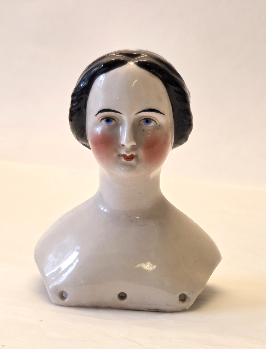 Porslin, vitglaserad. Rosa kinder. Svart hår. Blåa och svarta ögon. Röd mun. Vit och blå ettikett med "53".
Från Hedvig Ulfsparre.