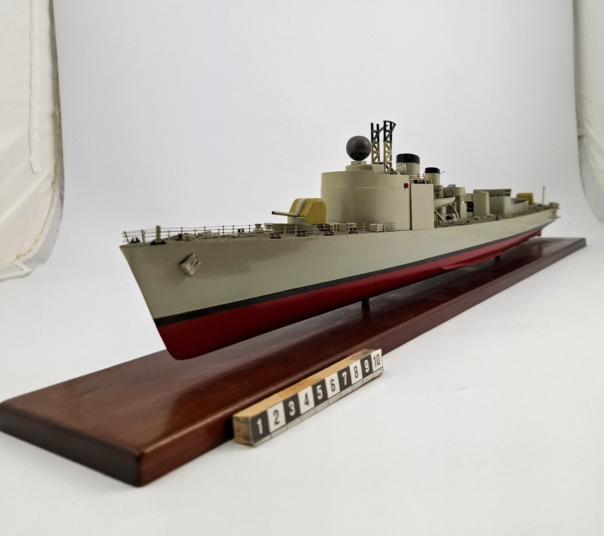 Fartygsmodell, huvudsaklingen gjord av trä med detaljer i plast och metall. Fartyget föreställer med högsta sannolikhet fregatten Sundsvall (1965-1982), tidigare stadsjagare (1942-1965). Modellen är målad grå över vattenlinjen, med en avskiljande svart linje och en röd bottenfärg. På fördäck står en kanon som är bemålad i gulaktig grön färg. På akterdäck finns en likadan kanon. Det finns två skorstenar med svarta toppar och ovanför styrhytten finns en ställning med grå botten och svart överkant som är trasig i toppen. I akterdelen finns en helikopterplatta och fartyget har tidigare haft två propellrar varav propellern på vänster sida är borta. Runt däcket finns en reling tillverkad i metall som omger hela fartyget. Modellen står på en fernissad platta av trä med hjälp av två kraftiga skruvar.