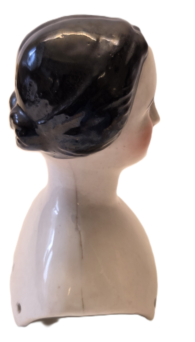 Porslin, vitglaserad. Rosa kinder. Svart hår. Blåa och svarta ögon. Röd mun. Vit och blå ettikett med "53".
Från Hedvig Ulfsparre.