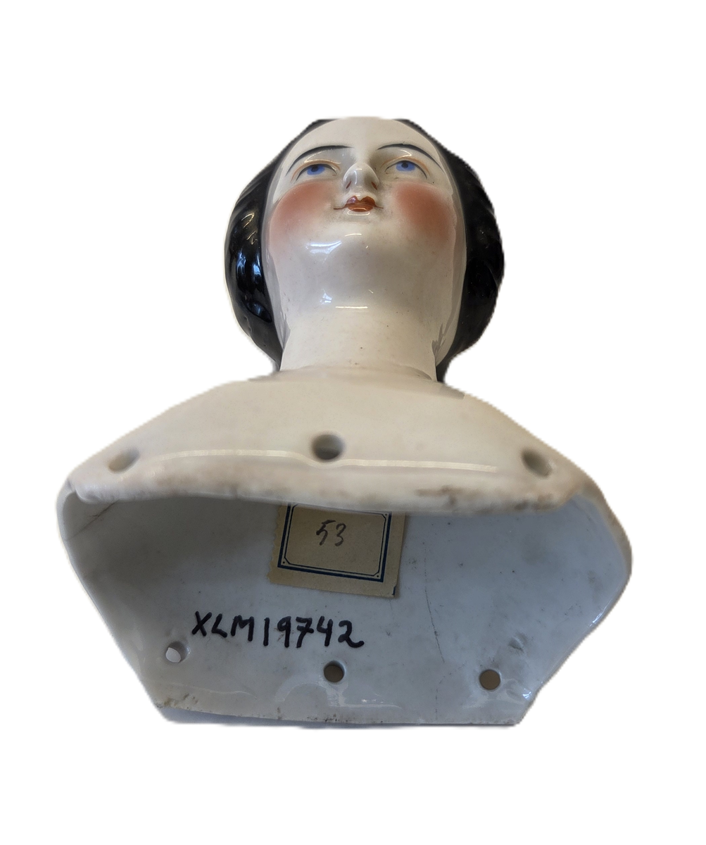 Porslin, vitglaserad. Rosa kinder. Svart hår. Blåa och svarta ögon. Röd mun. Vit och blå ettikett med "53".
Från Hedvig Ulfsparre.