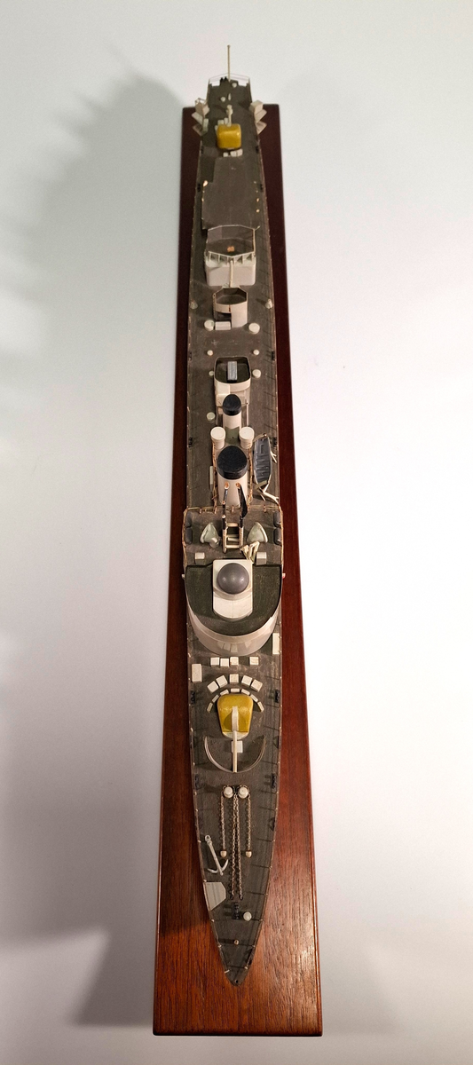 Fartygsmodell, huvudsaklingen gjord av trä med detaljer i plast och metall. Fartyget föreställer med högsta sannolikhet fregatten Sundsvall (1965-1982), tidigare stadsjagare (1942-1965). Modellen är målad grå över vattenlinjen, med en avskiljande svart linje och en röd bottenfärg. På fördäck står en kanon som är bemålad i gulaktig grön färg. På akterdäck finns en likadan kanon. Det finns två skorstenar med svarta toppar och ovanför styrhytten finns en ställning med grå botten och svart överkant som är trasig i toppen. I akterdelen finns en helikopterplatta och fartyget har tidigare haft två propellrar varav propellern på vänster sida är borta. Runt däcket finns en reling tillverkad i metall som omger hela fartyget. Modellen står på en fernissad platta av trä med hjälp av två kraftiga skruvar.