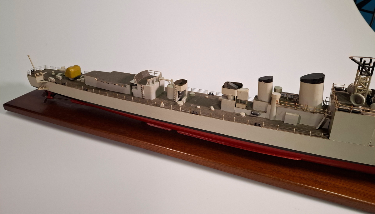 Fartygsmodell, huvudsaklingen gjord av trä med detaljer i plast och metall. Fartyget föreställer med högsta sannolikhet fregatten Sundsvall (1965-1982), tidigare stadsjagare (1942-1965). Modellen är målad grå över vattenlinjen, med en avskiljande svart linje och en röd bottenfärg. På fördäck står en kanon som är bemålad i gulaktig grön färg. På akterdäck finns en likadan kanon. Det finns två skorstenar med svarta toppar och ovanför styrhytten finns en ställning med grå botten och svart överkant som är trasig i toppen. I akterdelen finns en helikopterplatta och fartyget har tidigare haft två propellrar varav propellern på vänster sida är borta. Runt däcket finns en reling tillverkad i metall som omger hela fartyget. Modellen står på en fernissad platta av trä med hjälp av två kraftiga skruvar.