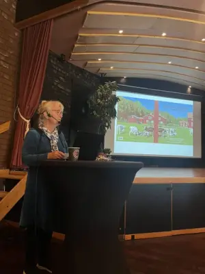 Kvinna som står vid podium med bildskärm i bakgrunden.