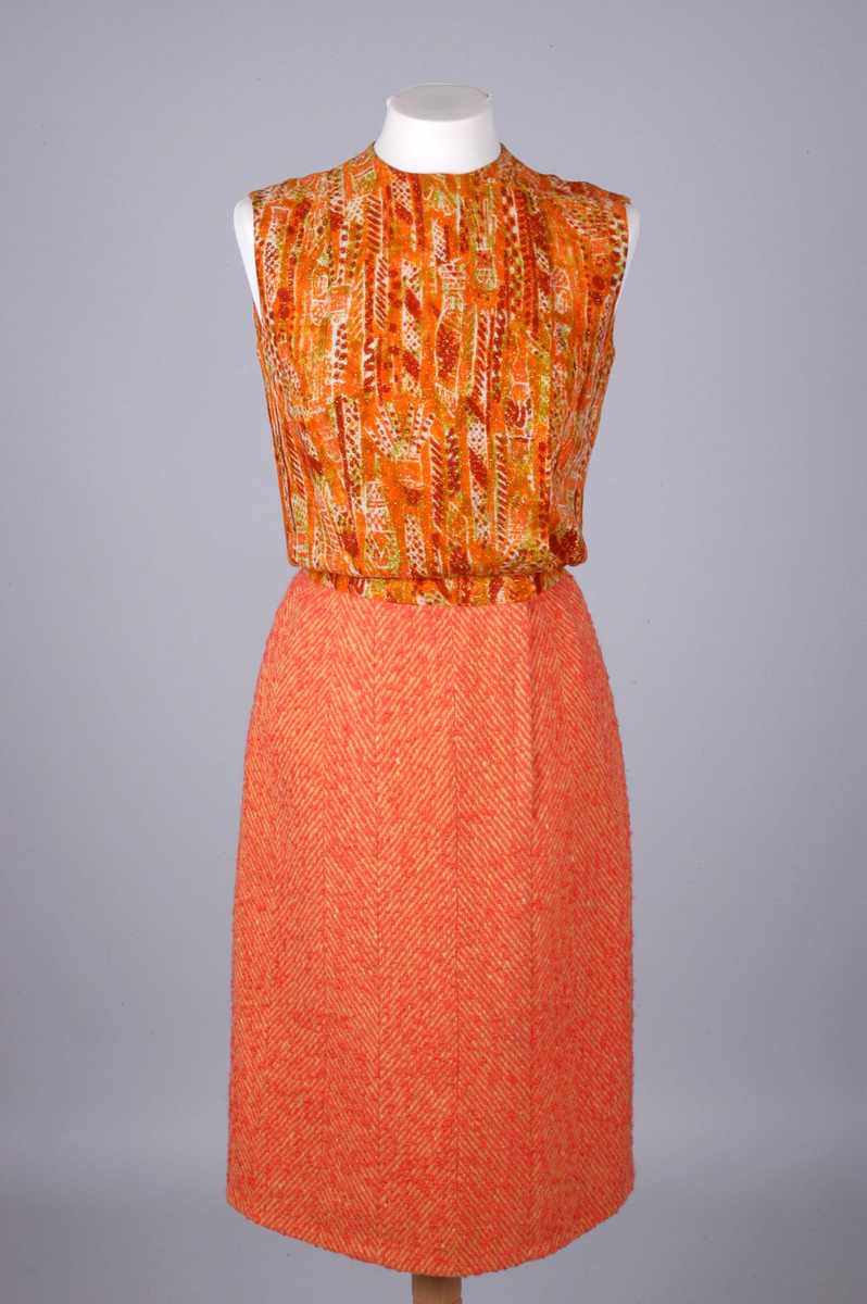 Todelt drakt bestående av kjole og jakke i korallfarget, fiskebensmønstret ull. Kjolen er konstruert slik at den ser ut som skjørt og bluse, og antrekket virker derfor tredelt. Det ermeløse kjolelivet har hel front og asymmetrisk lukking langs venstre skuldersøm og side. "Blusestoffet" er mønstret med gullfarget innslag. Skjørtet er fôret med silkestoff. Kjolelivet har svettelapper i silke. Jakken har pyntebånd i korall og gull, fire små lommer og gullfargede pynteknapper. Nederst på innsiden en påsydd gullfarget metallkjede. Fôret med korallfarget og sennepsgul silke.