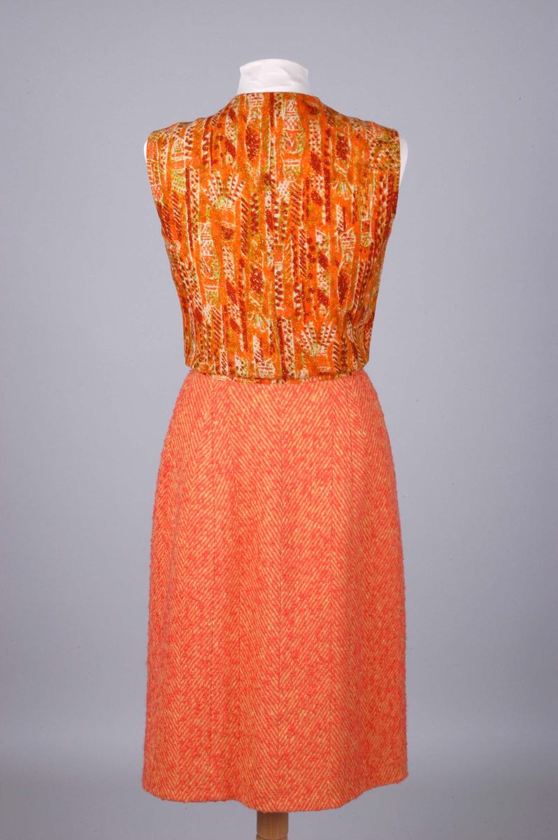 Todelt drakt bestående av kjole og jakke i korallfarget, fiskebensmønstret ull. Kjolen er konstruert slik at den ser ut som skjørt og bluse, og antrekket virker derfor tredelt. Det ermeløse kjolelivet har hel front og asymmetrisk lukking langs venstre skuldersøm og side. "Blusestoffet" er mønstret med gullfarget innslag. Skjørtet er fôret med silkestoff. Kjolelivet har svettelapper i silke. Jakken har pyntebånd i korall og gull, fire små lommer og gullfargede pynteknapper. Nederst på innsiden en påsydd gullfarget metallkjede. Fôret med korallfarget og sennepsgul silke.