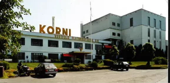 Bildet viser et hvitt næringsbygg med et stort skilt med oransje bokstaver på taket. Det står KORNI. På veggen under står det Vestfold flatbrødfabrikk AS  
