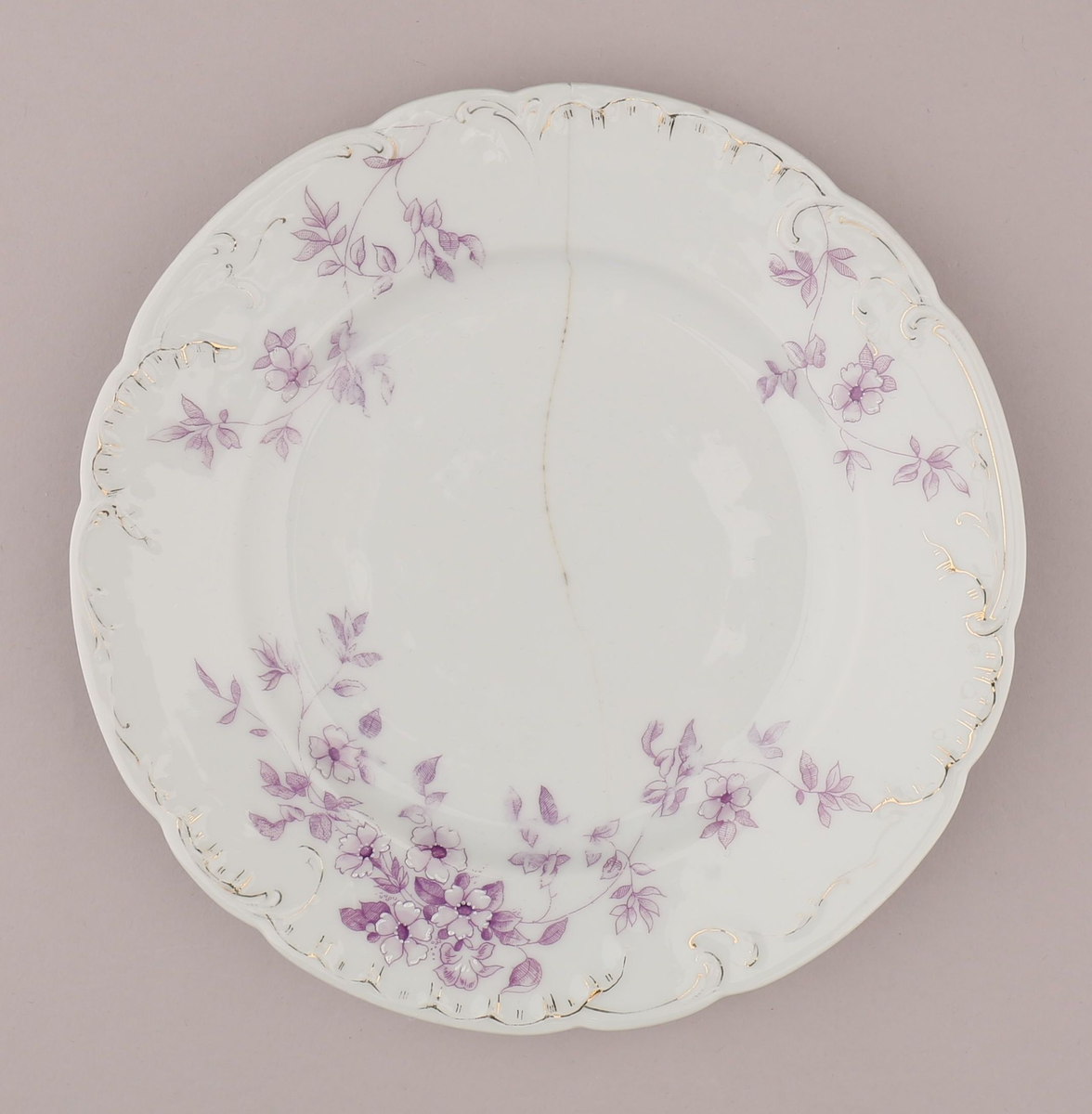 Rocaille og blomstermotiv bestående av blomster, blader, ranker, stengler. Motiv dekorert med tynn strek i fiolett nyanse med skraverte og åpne felt. Mørke fruktknute, lyse kronblader, skraverte blader i forskjellig mønster og alt fra lyse til mørke i fargen. Hvitt pigment benyttet for kontrast nær fruktknuten og ytterst på kronbladene.