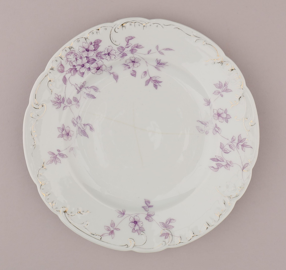 Rocaille og blomstermotiv bestående av blomster, blader, ranker, stengler. Motiv dekorert med tynn strek i fiolett nyanse med skraverte og åpne felt. Mørke fruktknute, lyse kronblader, skraverte blader i forskjellig mønster og alt fra lyse til mørke i fargen. Hvitt pigment benyttet for kontrast nær fruktknuten og ytterst på kronbladene.