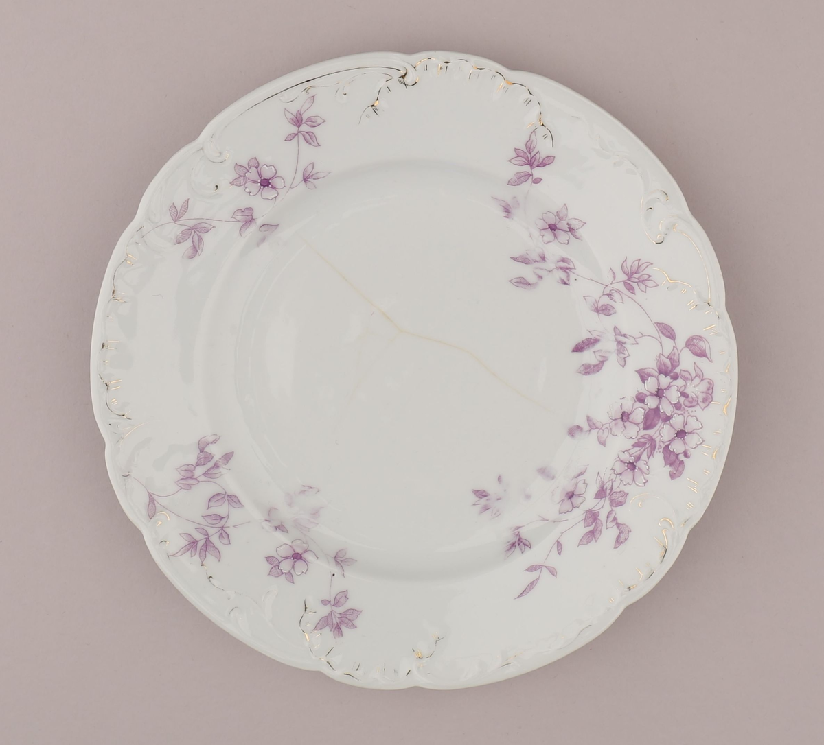 Rocaille og blomstermotiv bestående av blomster, blader, ranker, stengler. Motiv dekorert med tynn strek i fiolett nyanse med skraverte og åpne felt. Mørke fruktknute, lyse kronblader, skraverte blader i forskjellig mønster og alt fra lyse til mørke i fargen. Hvitt pigment benyttet for kontrast nær fruktknuten og ytterst på kronbladene.