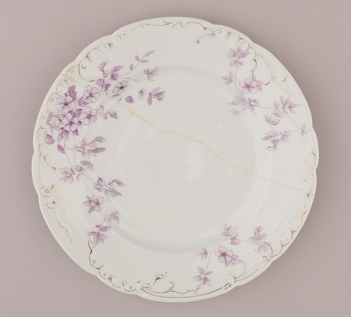 Rocaille og blomstermotiv bestående av blomster, blader, ranker, stengler. Motiv dekorert med tynn strek i fiolett nyanse med skraverte og åpne felt. Mørke fruktknute, lyse kronblader, skraverte blader i forskjellig mønster og alt fra lyse til mørke i fargen. Hvitt pigment benyttet for kontrast nær fruktknuten og ytterst på kronbladene.