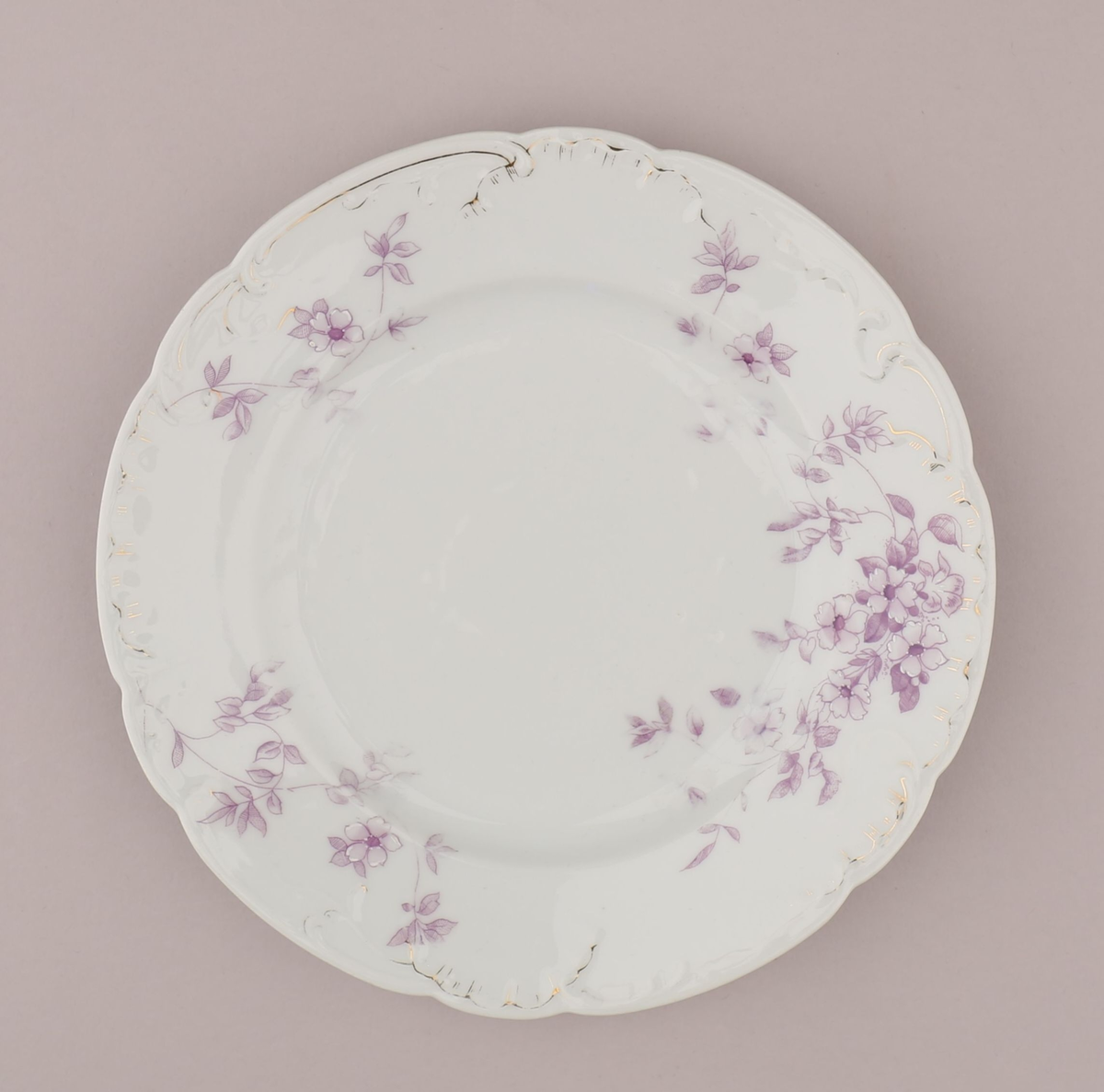 Rocaille og blomstermotiv bestående av blomster, blader, ranker, stengler. Motiv dekorert med tynn strek i fiolett nyanse med skraverte og åpne felt. Mørke fruktknute, lyse kronblader, skraverte blader i forskjellig mønster og alt fra lyse til mørke i fargen. Hvitt pigment benyttet for kontrast nær fruktknuten og ytterst på kronbladene.