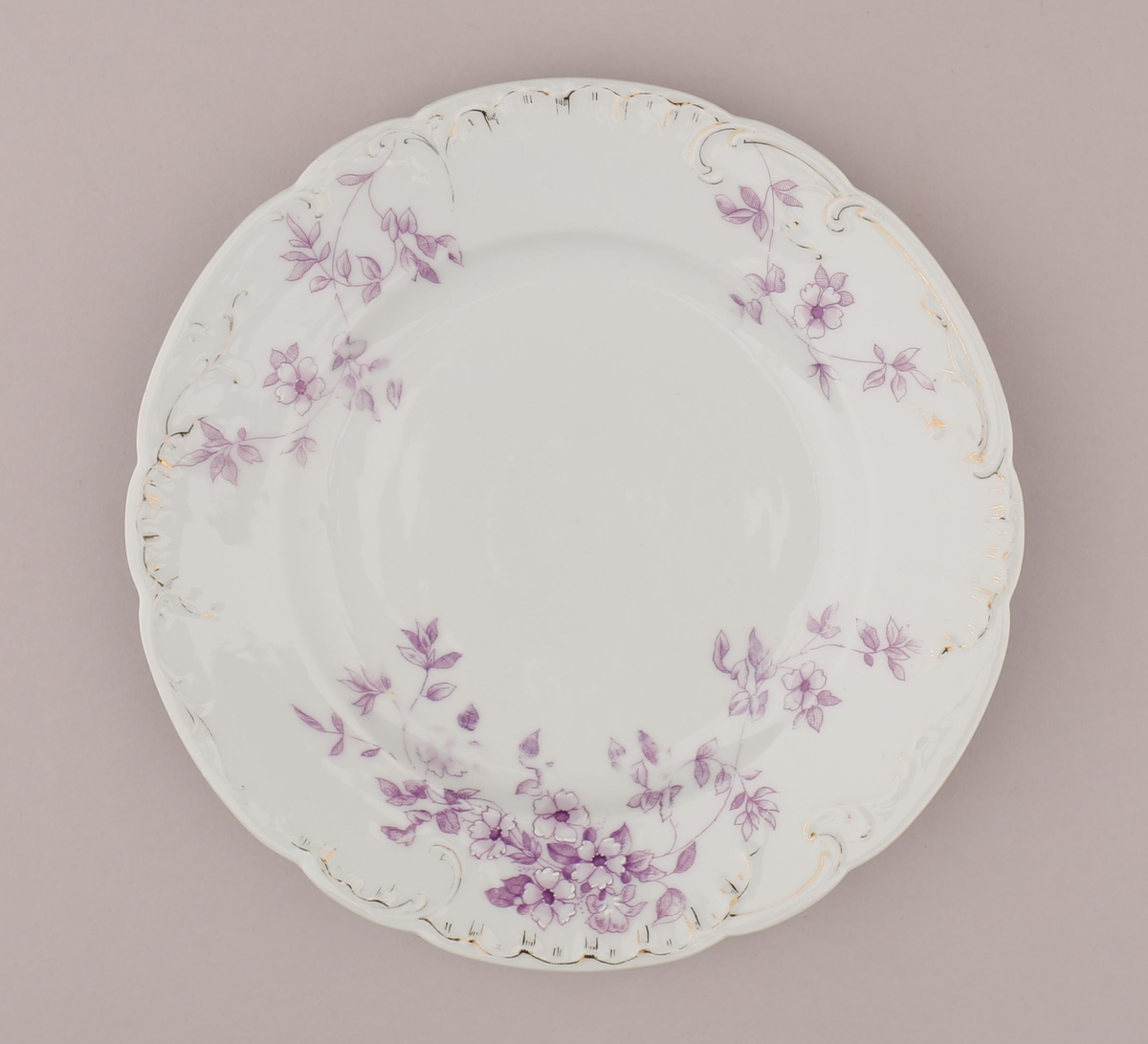 Rocaille og blomstermotiv bestående av blomster, blader, ranker, stengler. Motiv dekorert med tynn strek i fiolett nyanse med skraverte og åpne felt. Mørke fruktknute, lyse kronblader, skraverte blader i forskjellig mønster og alt fra lyse til mørke i fargen. Hvitt pigment benyttet for kontrast nær fruktknuten og ytterst på kronbladene.