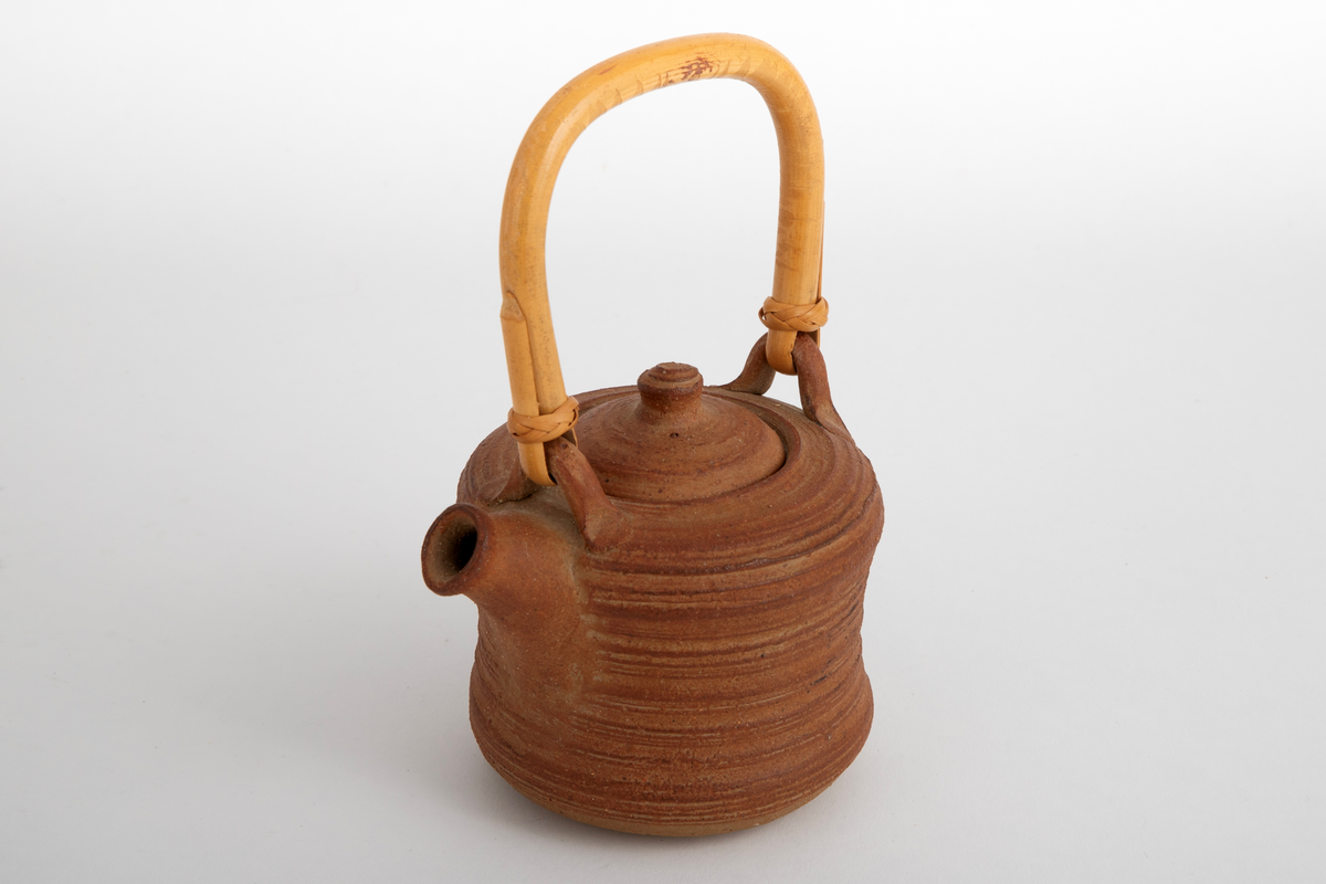Liten brun tekanne med lokk og trehåndtak. Kraftige riller etter dreiingen. Noe konkav på midten av korpus.