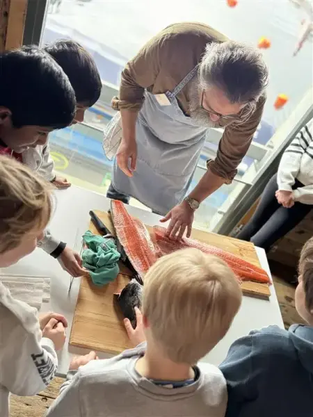 Vi ser kokken forklare om laksefileten som ligger foran han til en gruppe barn