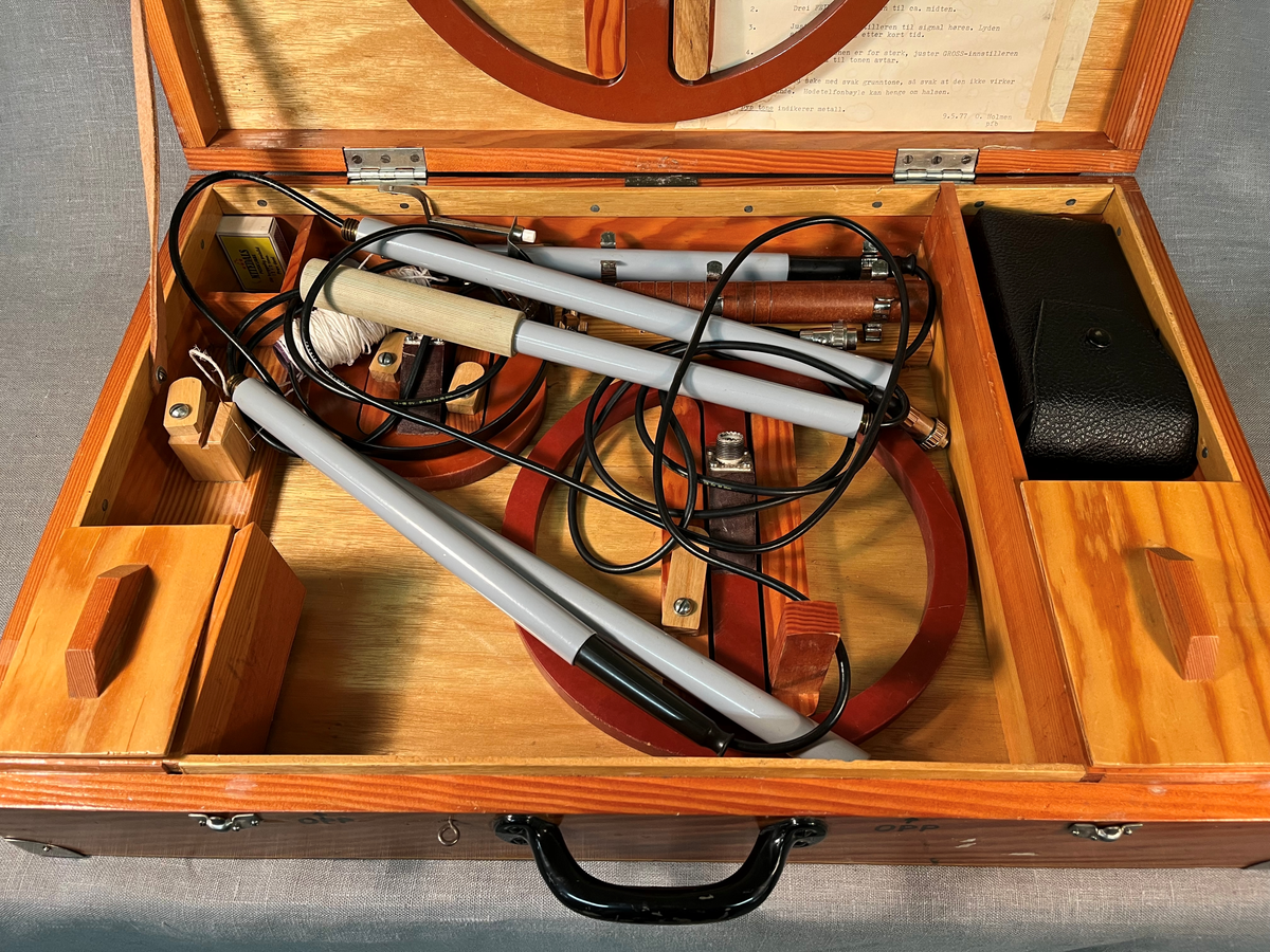 Sammenleggbar metalldetektor oppbevart i trekoffert. Bruksanvisning medfølger.