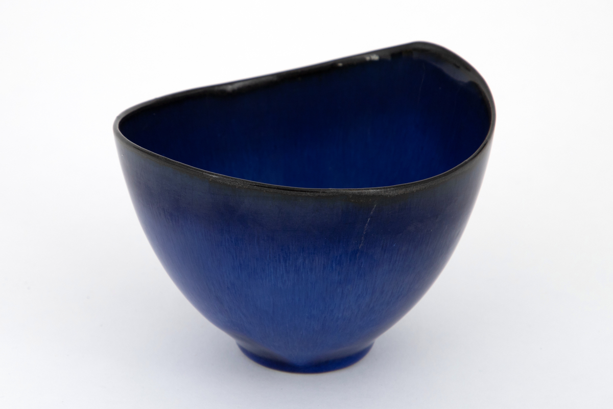 Skål i steingods, oval form med noe skjevt oppsvunget munningsrand i begge ender. Dekket med blank glasur i skiftende nyanser av blått, lysere blå mot bunnen og dypblå nærmere munningsranden.